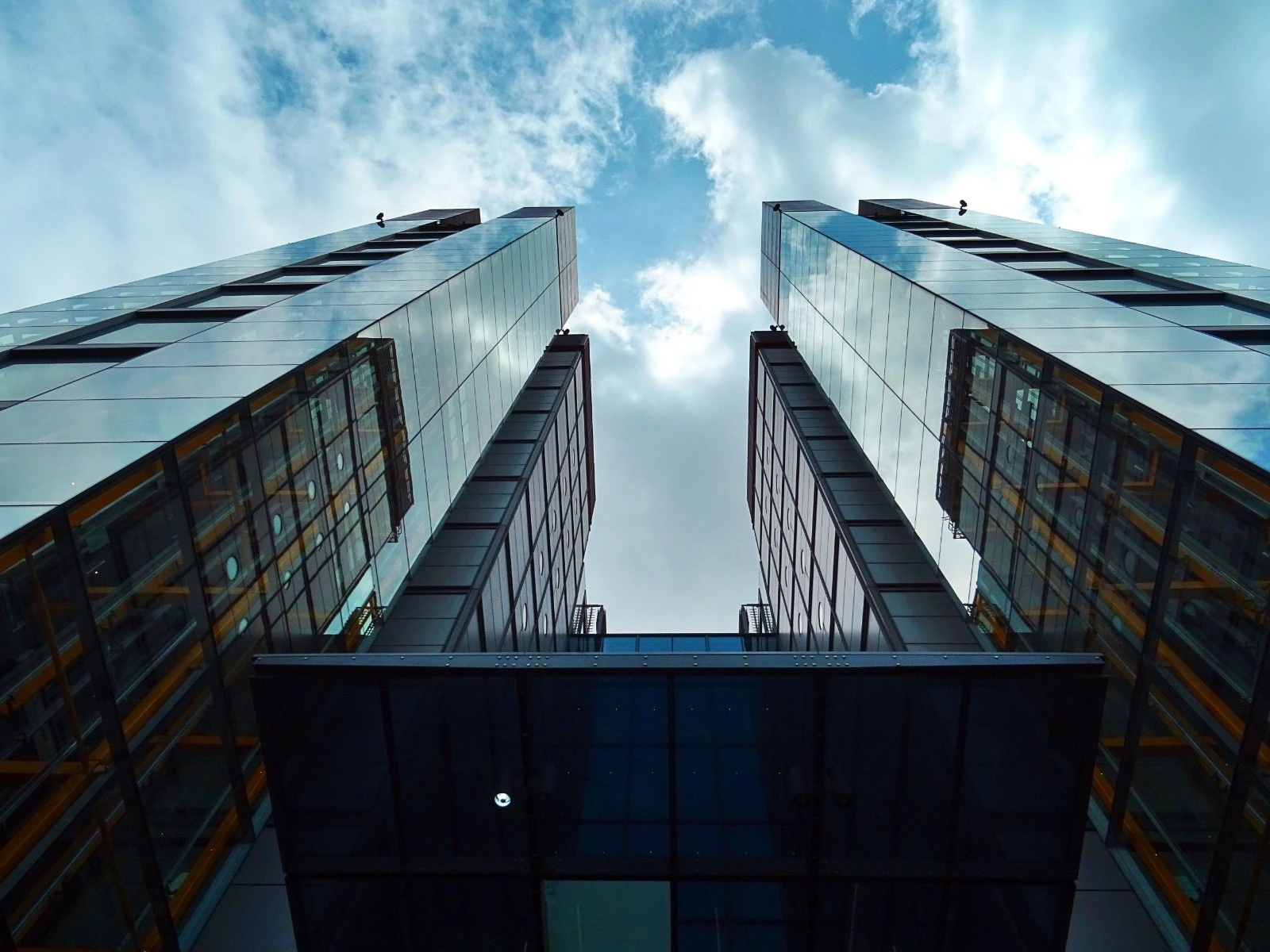 An upward view between two glass buildings framing an opening to the sky