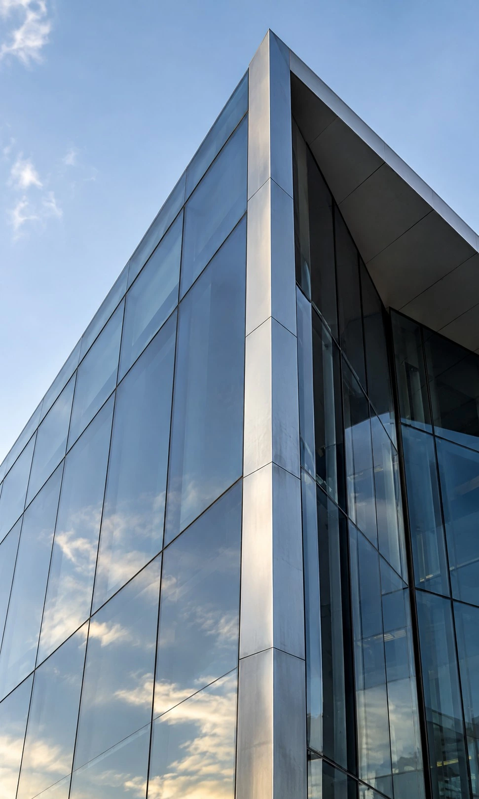 A silver-edged glass building corner rising into pale blue sky
